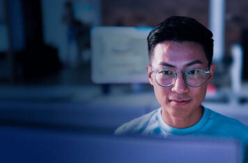 Man with glasses looking at monitor on desk