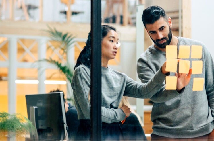 Woman and man reviewing post-it notes on interior office window.
