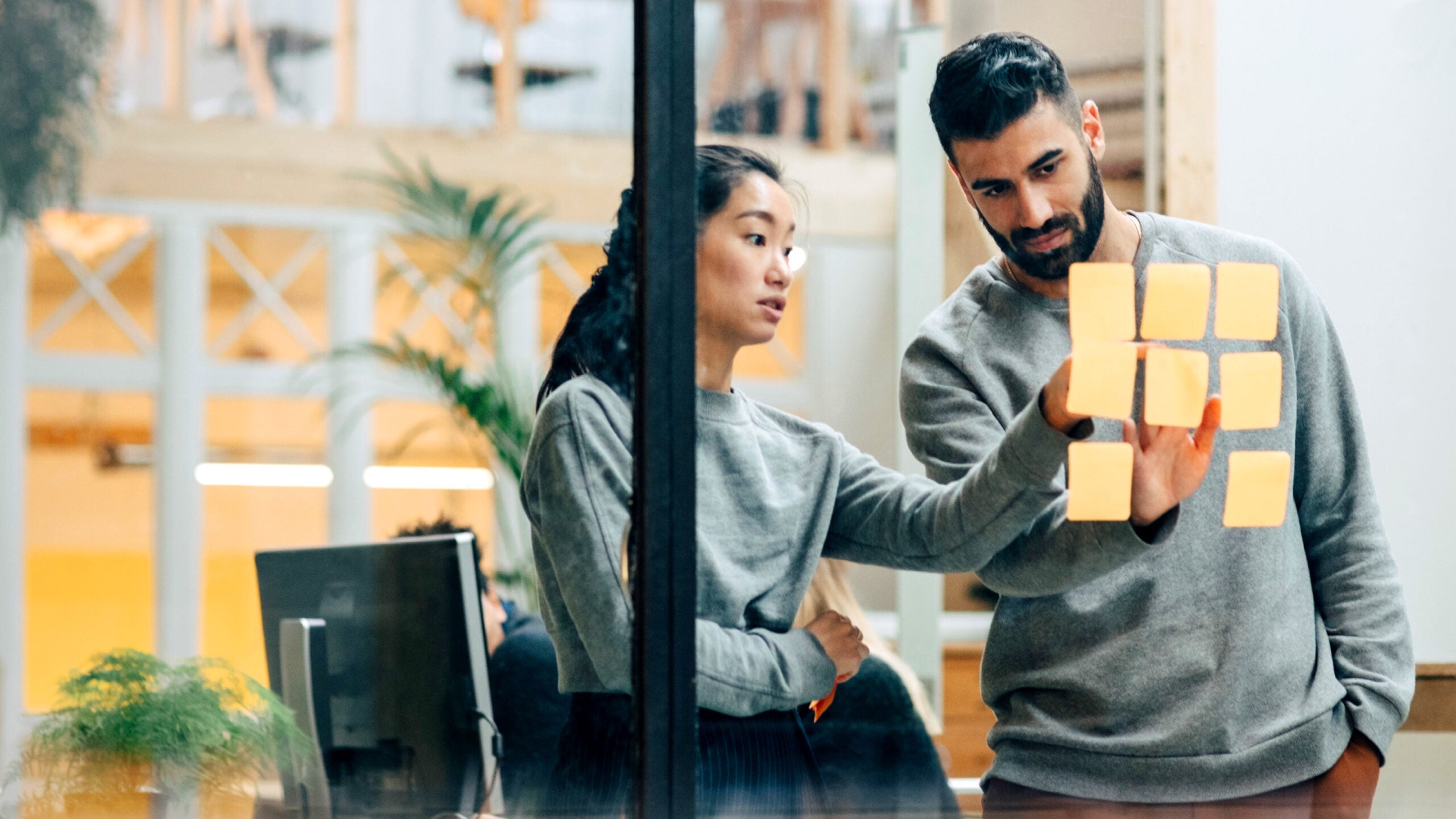 Woman and man reviewing post-it notes on interior office window.
